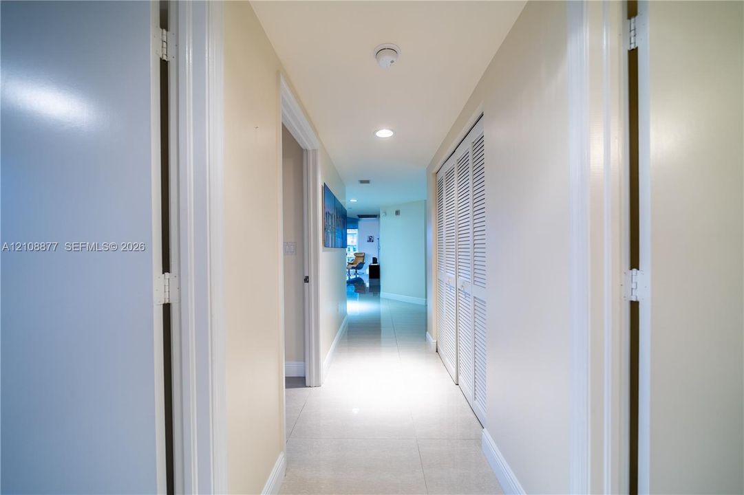 Hallway featuring light-toned tile flooring, recessed ceiling lighting, and built-in closet cabinetry with white louvered doors