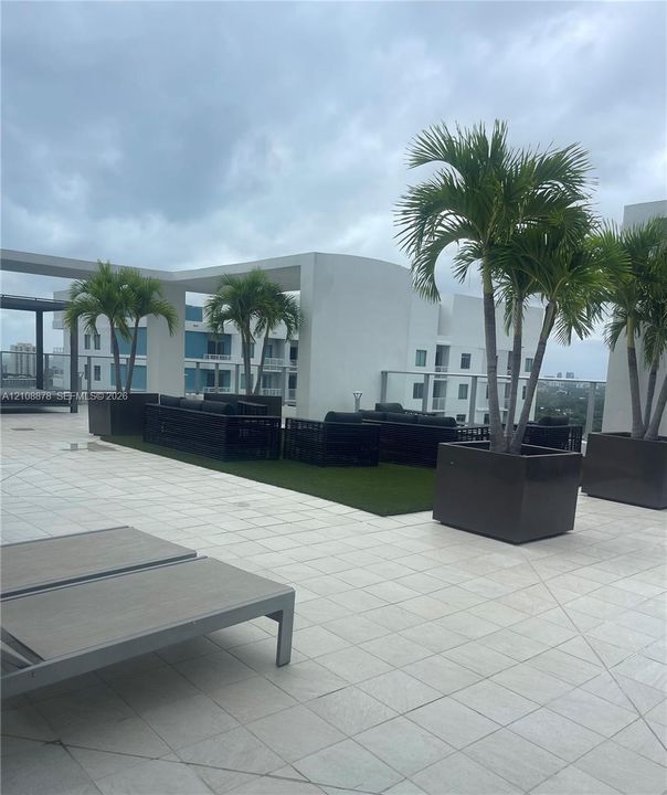 Expansive rooftop terrace featuring large-format stone tile flooring, structural architectural pillars, glass panel railing, and built-in planters with palms