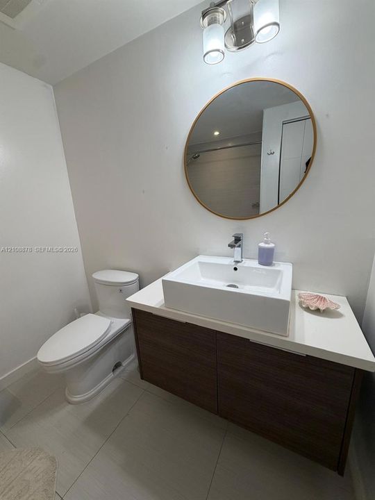 Floating wood-finish vanity with a white rectangular vessel sink, solid-surface countertop, round wall-mounted mirror, and sleek chrome fixtures