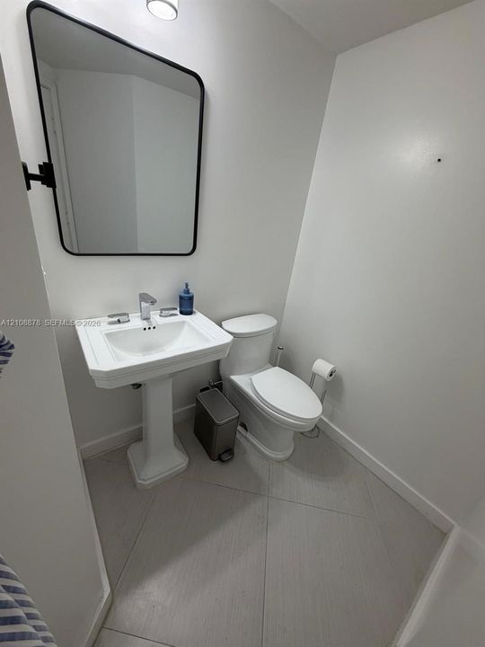 White pedestal sink with a chrome single-handle faucet, elongated toilet, rectangular wall mirror with a matte black frame, and large-format tile flooring