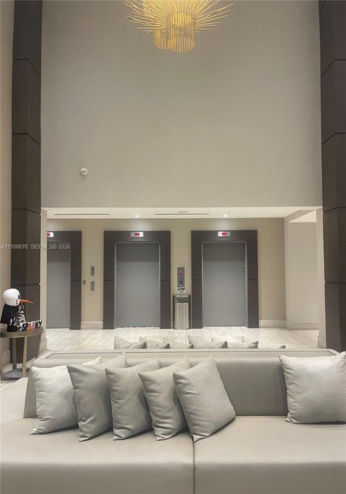 Lobby featuring vaulted ceilings, a structural sunburst chandelier, natural stone flooring, and a bank of three elevators with dark-toned frames