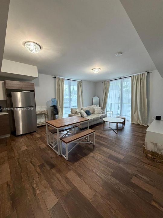 Open-concept interior featuring wood-finish flooring, stainless steel refrigerator, and recessed ceiling lighting