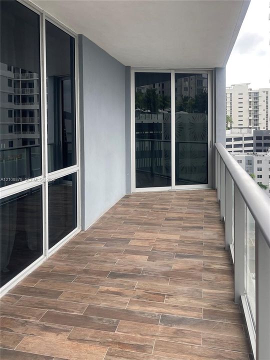 Covered balcony featuring wood-finish tile flooring, glass panel railings, and floor-to-ceiling sliding glass doors