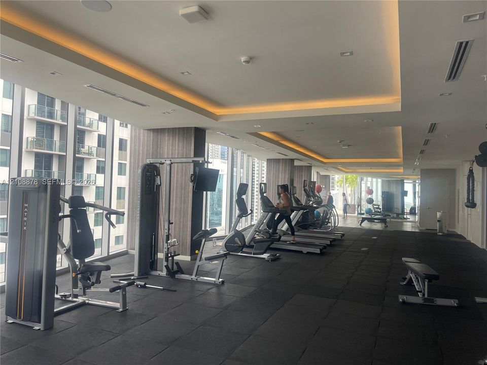 Fitness center featuring floor-to-ceiling windows, tray ceilings with integrated cove lighting, recessed lighting, and rubberized flooring