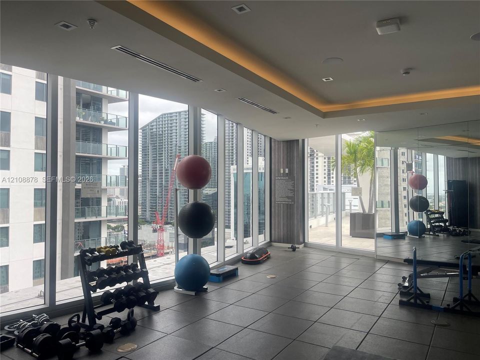 Fitness center featuring floor-to-ceiling glass windows, recessed tray ceiling lighting, dark large-format tile flooring, and mirrored wall panels