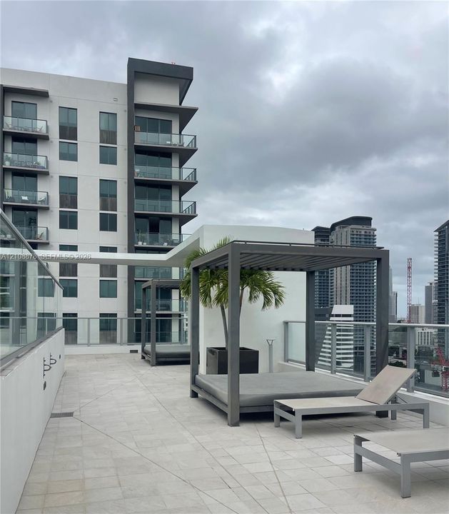 Rooftop terrace featuring light-colored stone tile flooring, metal frame cabanas, and glass panel railings