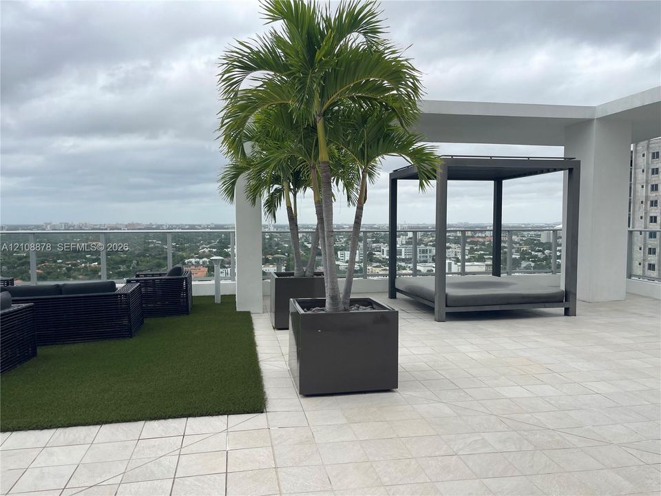 Rooftop terrace featuring large-format tile flooring, glass panel railings, and square built-in planters