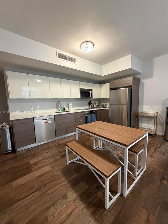 Kitchen featuring two-tone flat-panel cabinetry, white solid-surface countertops, stainless steel appliances, and wood-finish flooring