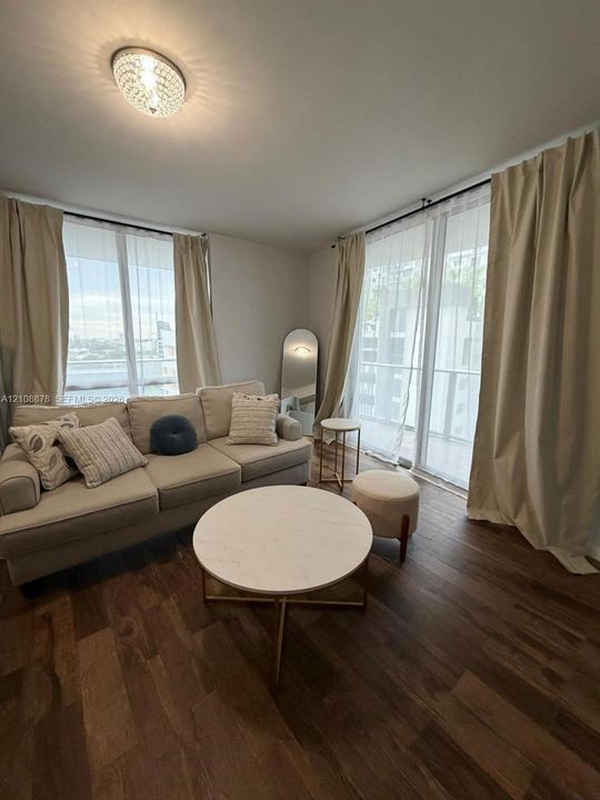 Wood-finish flooring, dual floor-to-ceiling windows, and a flush-mount crystal ceiling light fixture