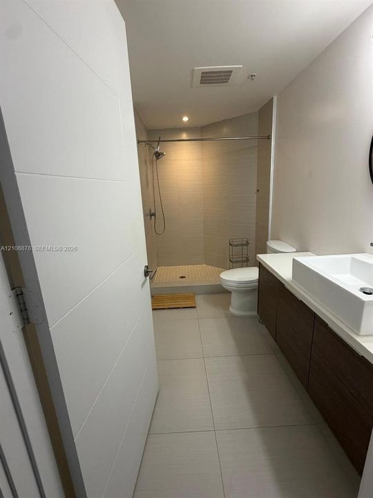 Bathroom featuring a floating wood-finish vanity, rectangular vessel sink, neutral floor tiling, and a tiled shower enclosure with a stainless steel shower head