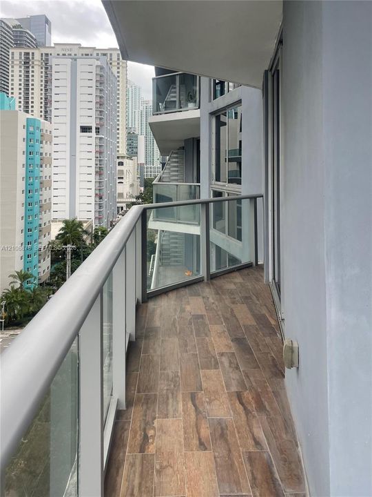Private balcony featuring wood-finish flooring and glass panel railings with metal framing