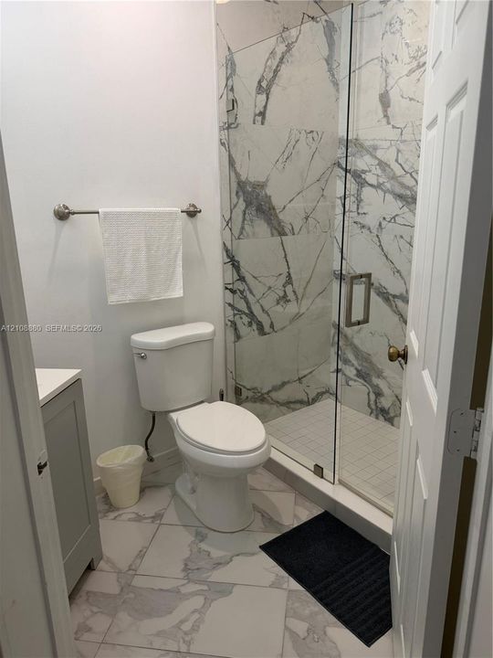 Walk-in shower with floor-to-ceiling large-format veined tile, frameless glass enclosure, and matching large-format tile flooring
