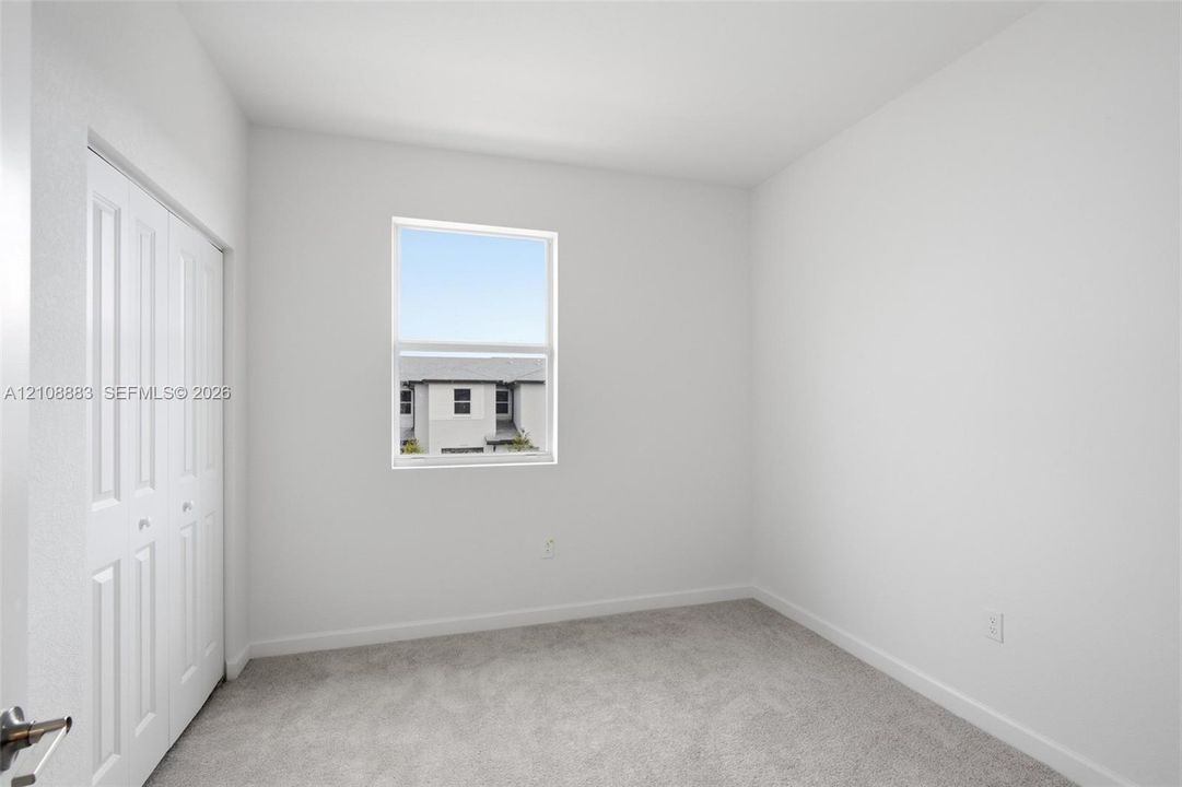 Neutral-toned interior space featuring light-colored wall-to-wall carpeting, white walls, and a closet with white bifold doors