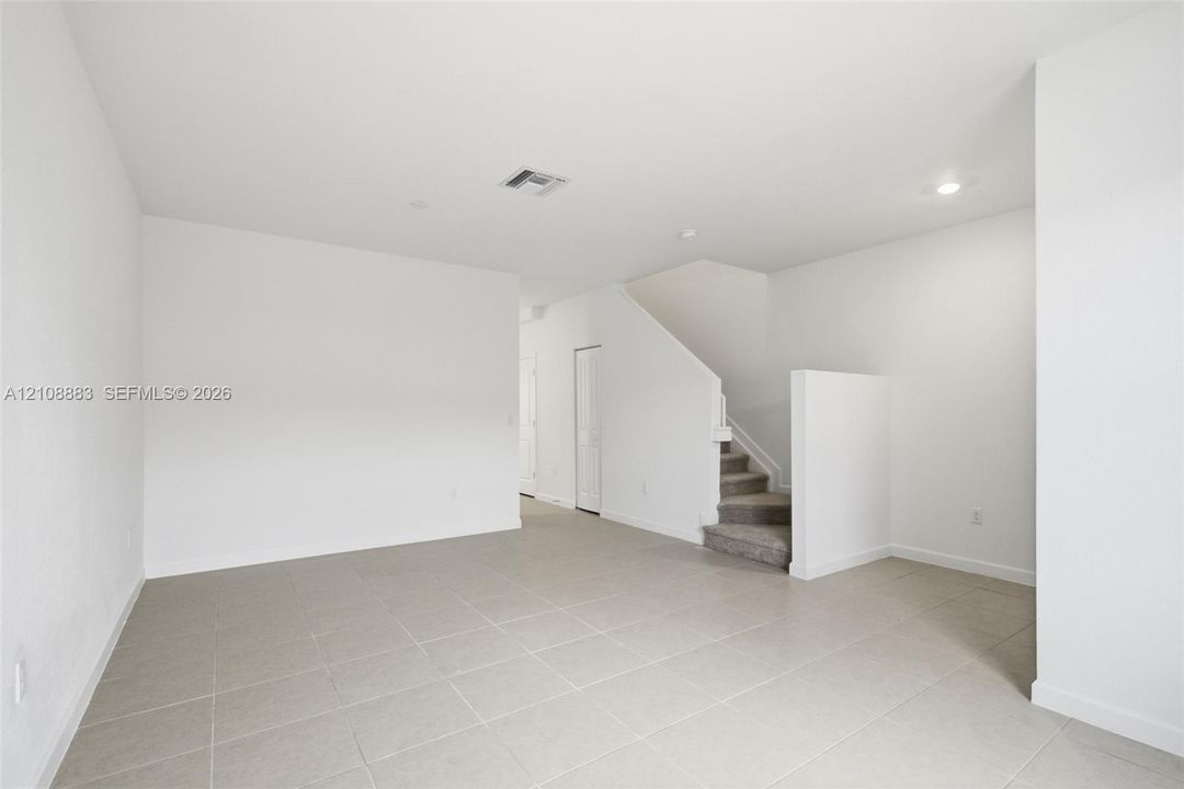 Neutral interior space featuring large-format ceramic tile flooring, recessed lighting, and a staircase with carpeted treads