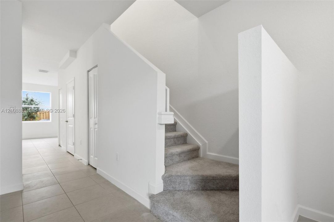 Foyer area featuring neutral ceramic tile flooring, carpeted staircase, and high-reaching walls