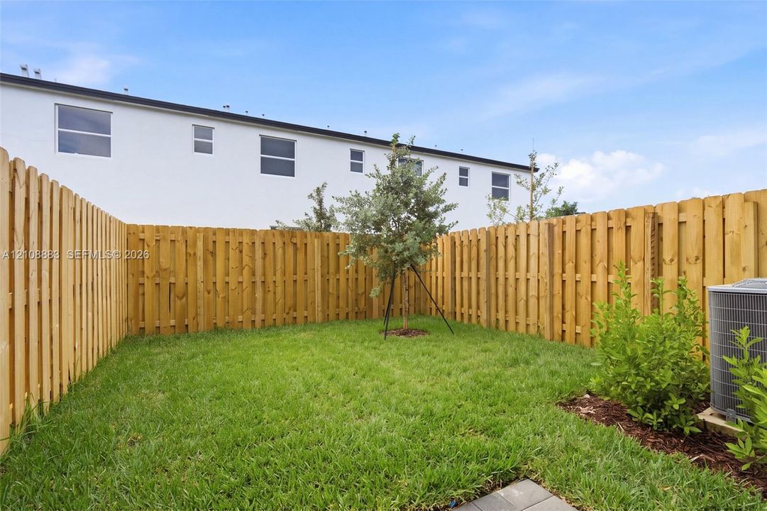 Rear yard featuring a manicured lawn, wood-panel fencing, and a central sapling