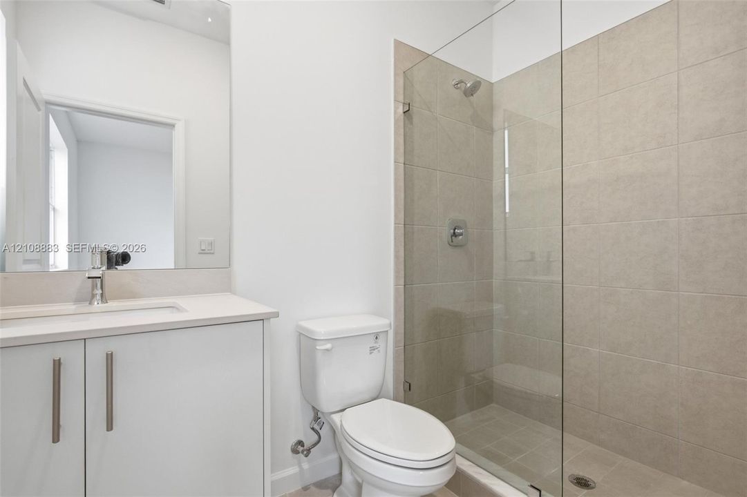 Bathroom featuring a vanity with a white countertop and rectangular sink, a wall-to-wall mirror, a floor-mounted toilet, and a glass-enclosed shower with neutral-toned wall tile