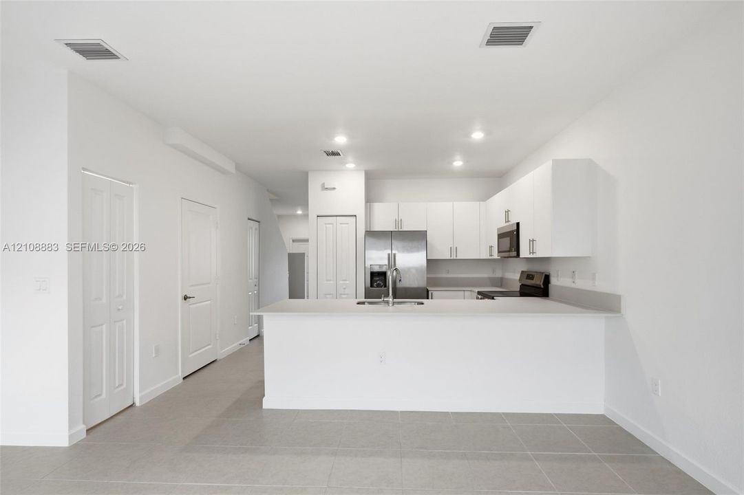 Kitchen featuring white flat-panel cabinetry, a peninsula with stone-surface countertop, stainless steel refrigerator, built-in microwave, and large-format tile flooring