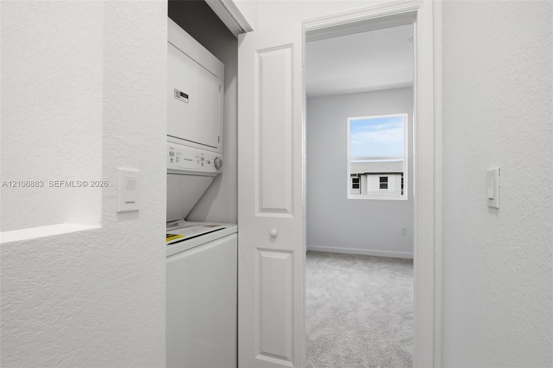 Stacked laundry unit with white appliances housed in a dedicated closet featuring a bi-fold door