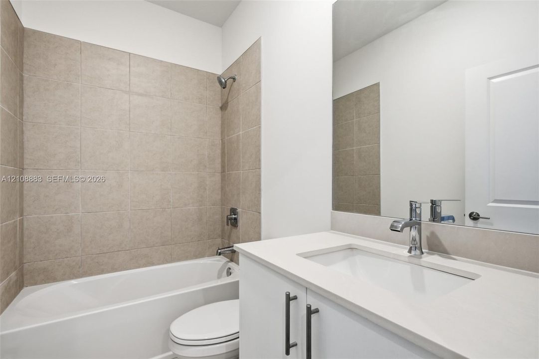 Bathroom featuring a white vanity with a composite countertop and integrated basin, a large wall-mounted mirror, and a tub-shower combination with floor-to-ceiling neutral tile surround