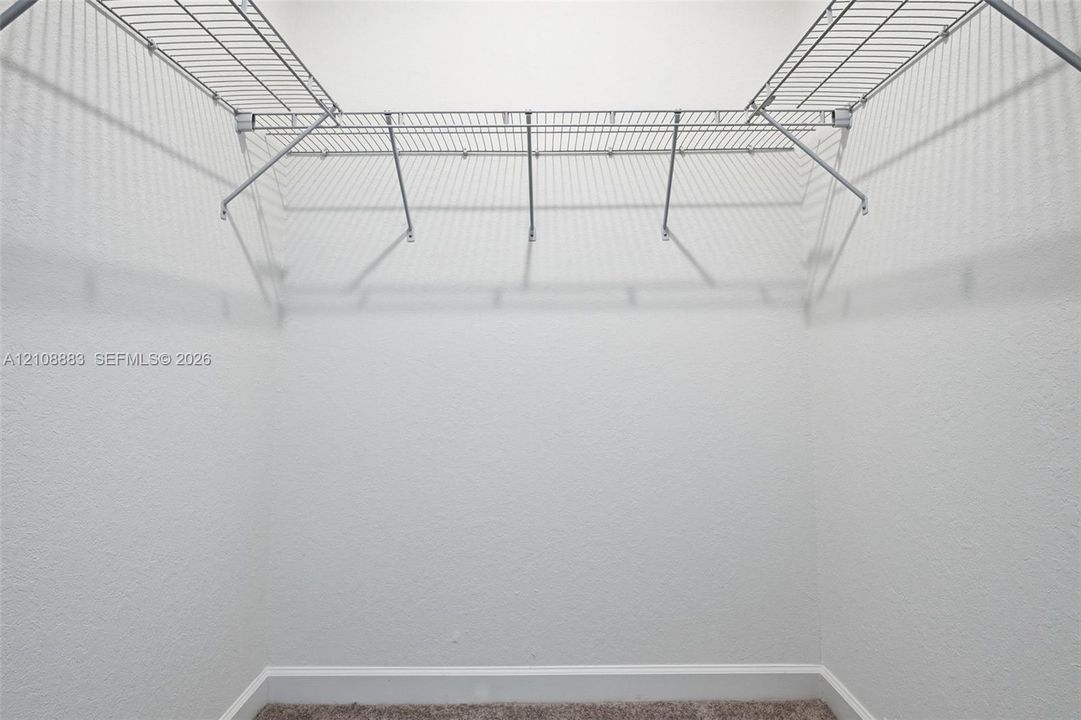 Storage area featuring white textured walls and integrated wire shelving with built-in garment rods