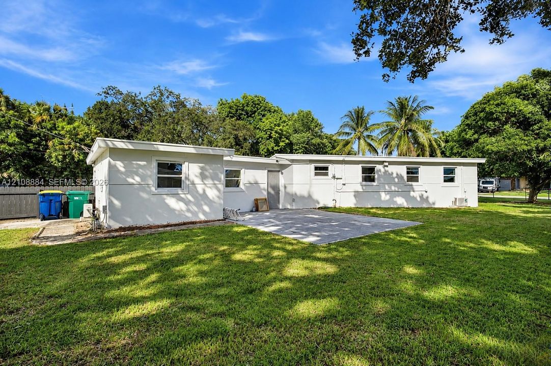 Exterior of the residence featuring a concrete patio, light-colored smooth finish siding, and mature trees on the grounds