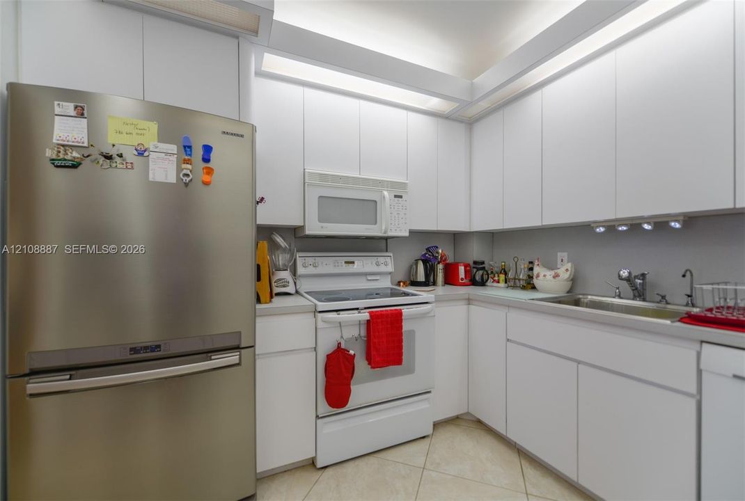 Kitchen featuring floor-to-ceiling white cabinetry, integrated recessed lighting, stainless steel refrigerator, white electric range with over-the-range microwave, and tile flooring