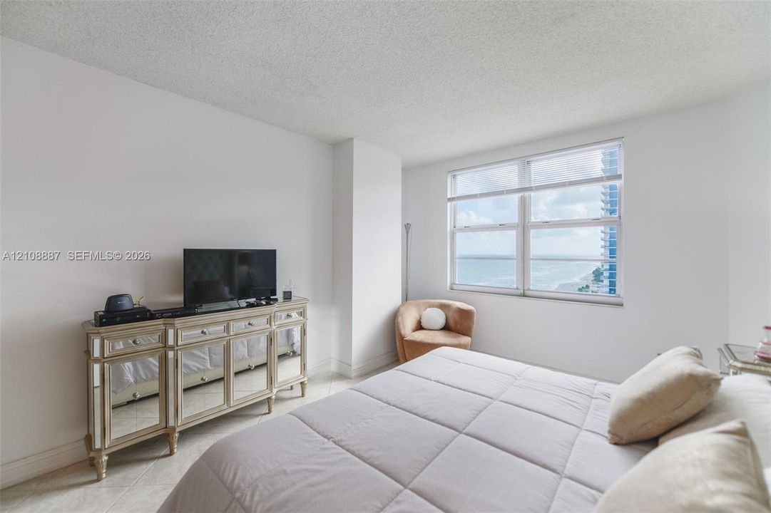 Neutral-toned interior featuring expansive horizontal windows with ocean and coastal horizon scenery, light-colored tile flooring, and textured ceiling finish