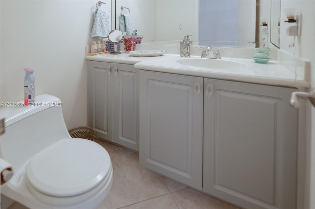 Bathroom vanity featuring soft-gray cabinetry, a white countertop, an integrated oval sink, chrome dual-handle faucet, and large-format tile flooring