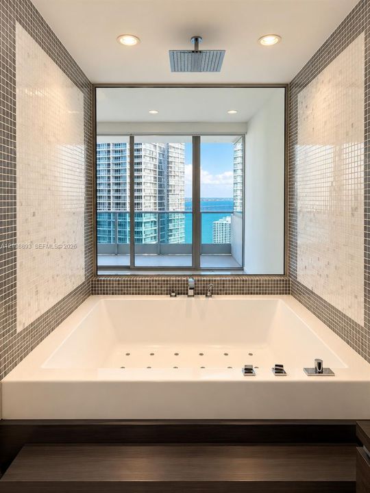 Drop-in soaking tub with a deck-mounted faucet, square rain shower head, large-format mirror, and custom mosaic tile surround