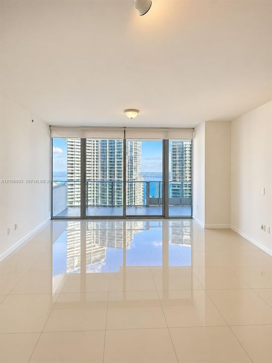 Floor-to-ceiling glass windows, ceramic tile flooring, and a glass-paneled balcony with panoramic water and skyline scenery