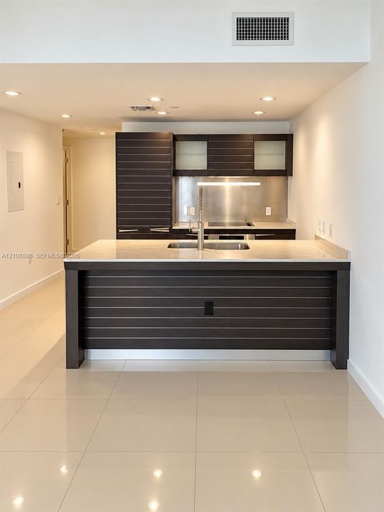 Kitchen featuring dark wood-finish cabinetry with horizontal slat detailing, stone-surface island countertop, integrated stainless steel backsplash, and polished tile flooring