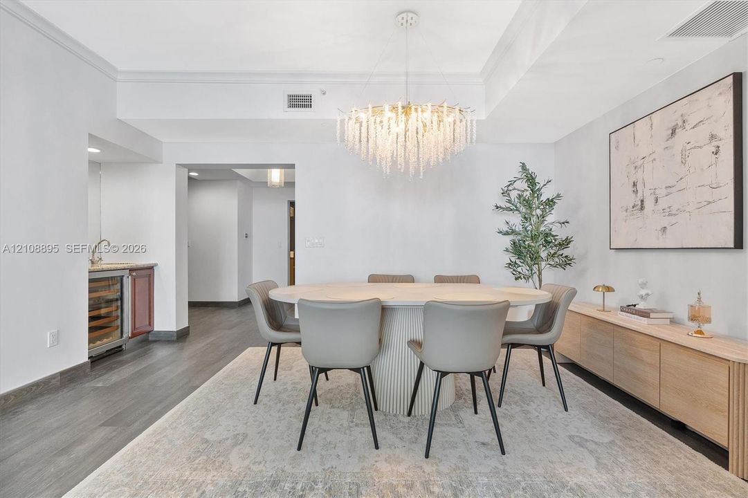 Dining area featuring wood-finish flooring, a tiered crystal chandelier, and a built-in wet bar with a glass-front beverage cooler