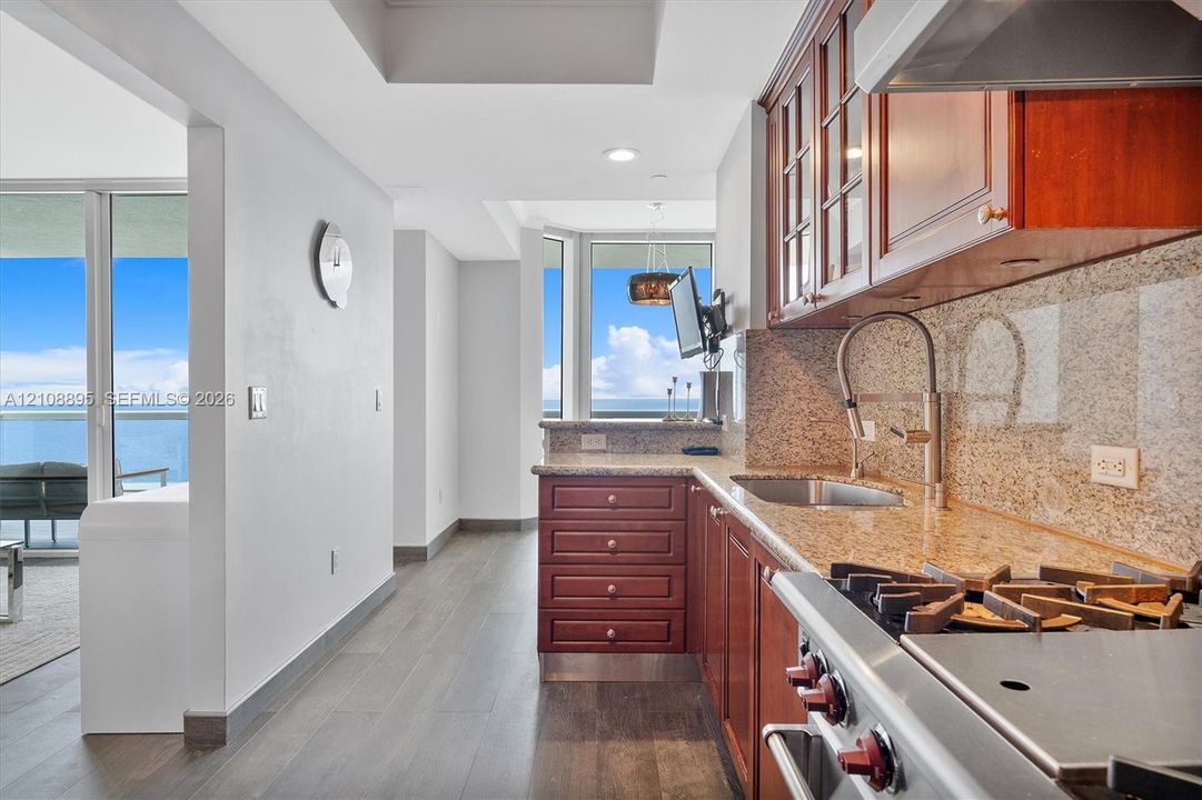 Kitchen featuring wood cabinetry, stone countertops, stainless steel gas range, stone backsplash, and wood-finish flooring