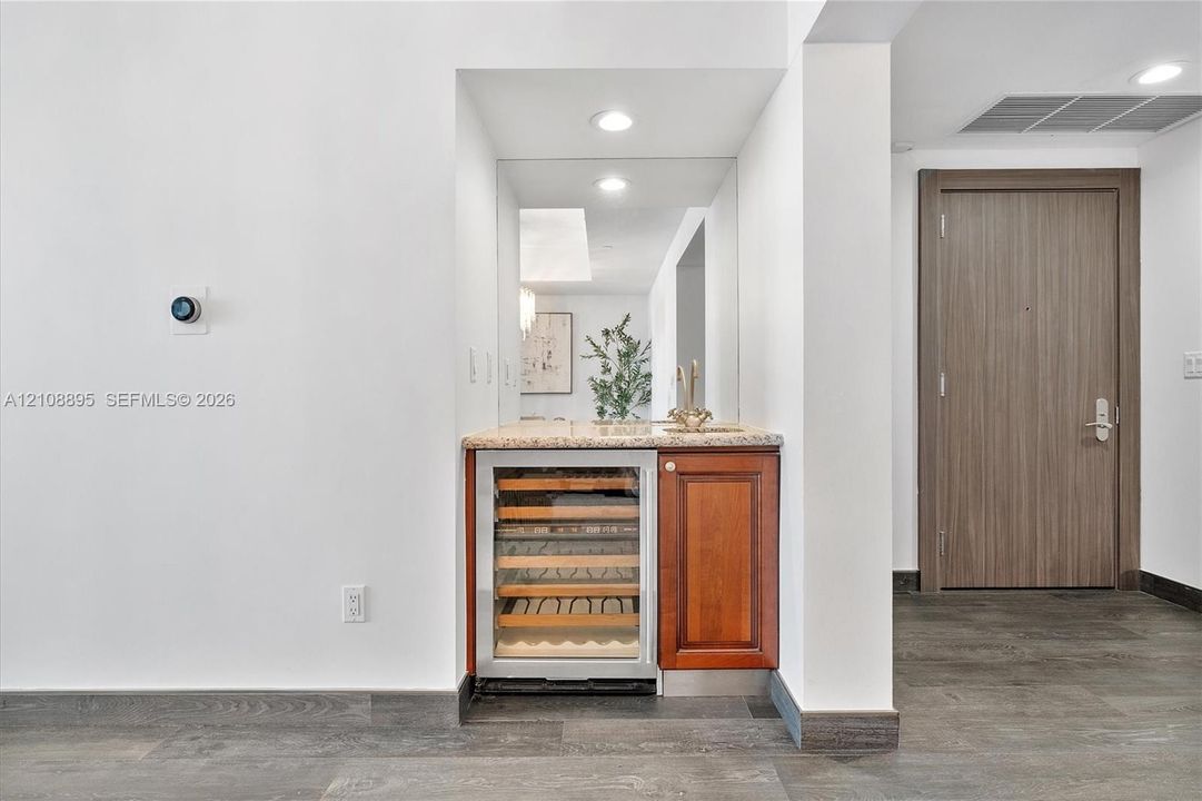 Built-in wet bar featuring a stone-topped counter, undermount sink, integrated wine refrigerator, and wood cabinetry