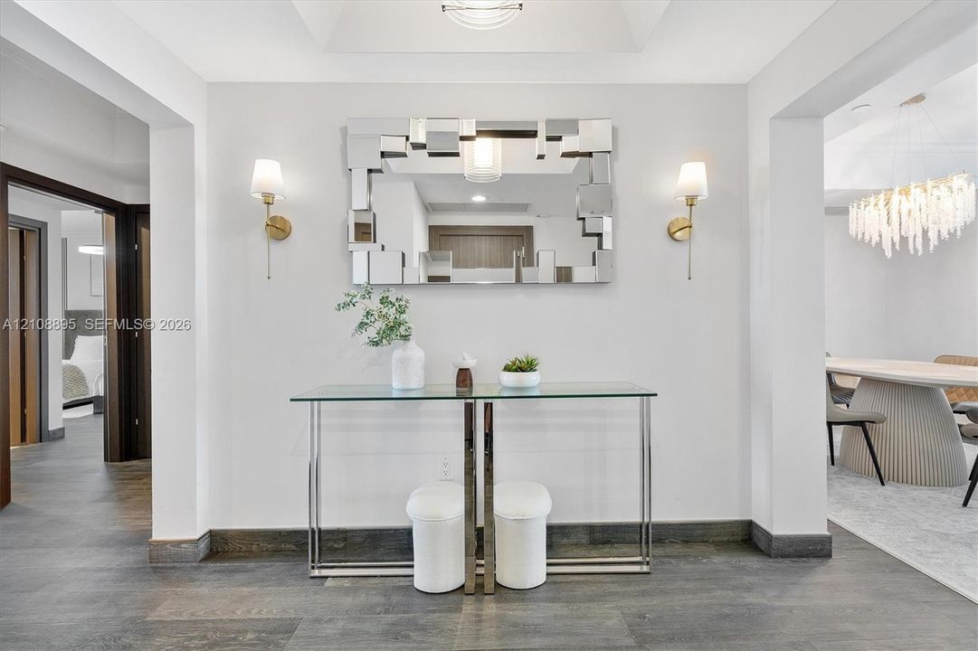 Foyer featuring wood-finish flooring, a tray ceiling, dual wall-mounted sconces, and a decorative mirror