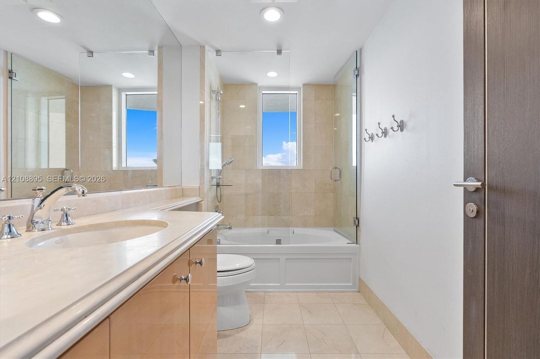 Bathroom featuring a vanity with integrated sink and stone-finish countertop, full-width mirror, soaking tub with glass enclosure, wall-mounted hardware, and tile flooring