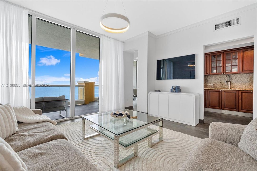 Floor-to-ceiling glass sliding doors, private balcony, wood-finish flooring, built-in wet bar with cabinetry, and modern circular pendant lighting