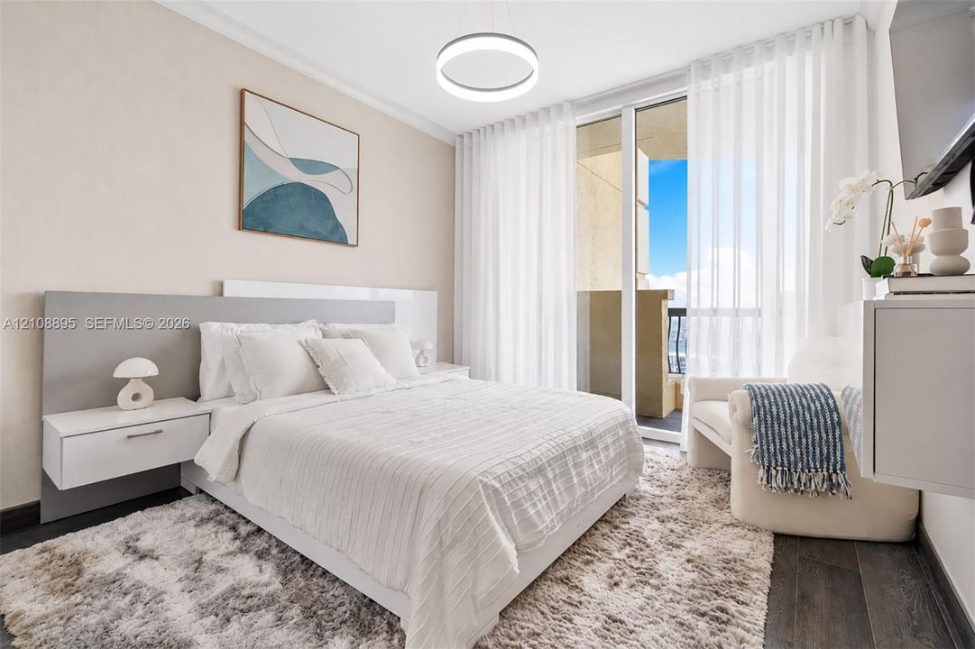Floor-to-ceiling glass sliding doors with balcony access, wood-finish flooring, integrated wall-mounted nightstands, circular pendant lighting, and a neutral-toned accent headboard panel