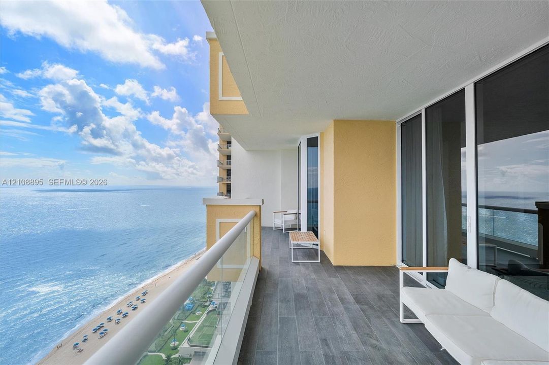 Covered balcony featuring wood-finish tile flooring, glass panel railings, and floor-to-ceiling windows