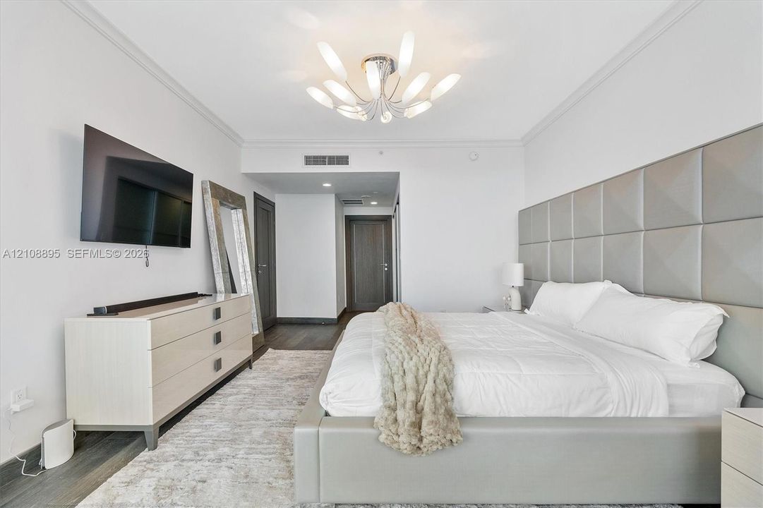 Custom floor-to-ceiling tufted headboard, multi-arm sculptural light fixture, wood-finish flooring, and crown molding