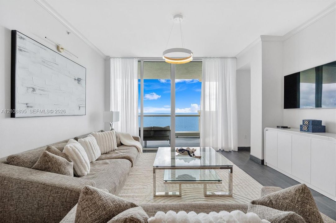 Living space featuring floor-to-ceiling glass sliding doors, dark wood-finish flooring, built-in cabinetry, circular pendant lighting, and an expansive balcony