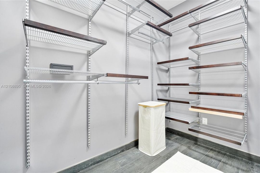 Customizable modular storage system featuring adjustable metal shelving with dark-toned wood trim and integrated hanging rods, complemented by dark wood-finish flooring