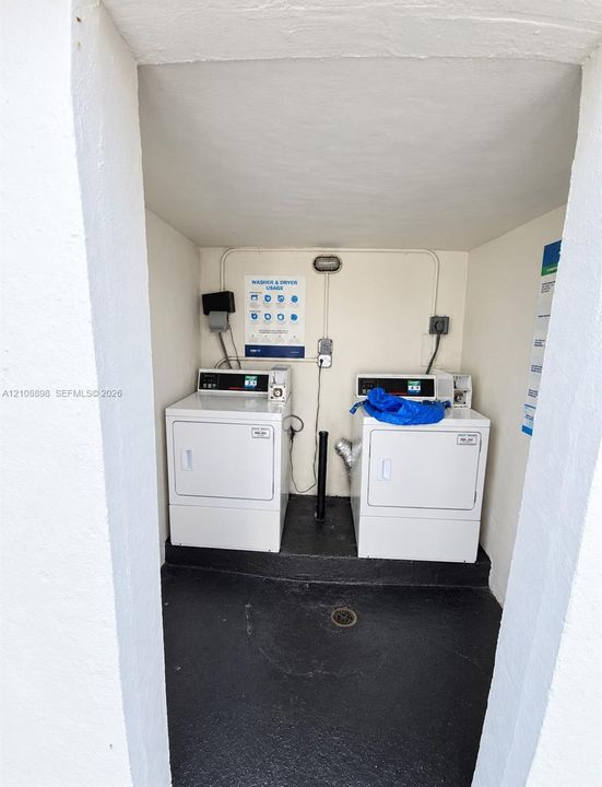 Dedicated laundry space featuring two white appliances, black flooring, and a floor drain