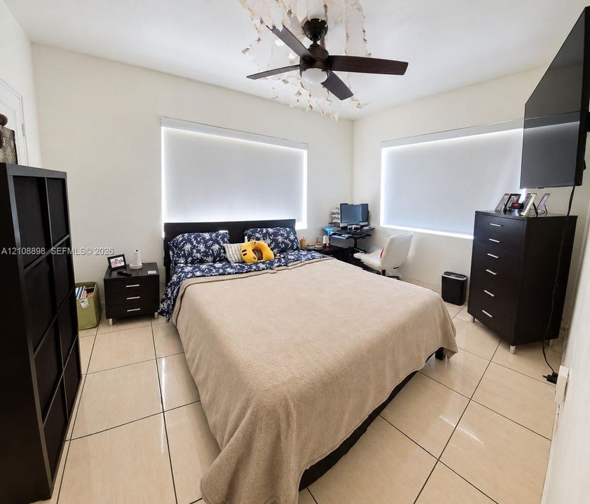 Large-format tile flooring, dual windows with fitted roller shades, and a ceiling fan with integrated lighting