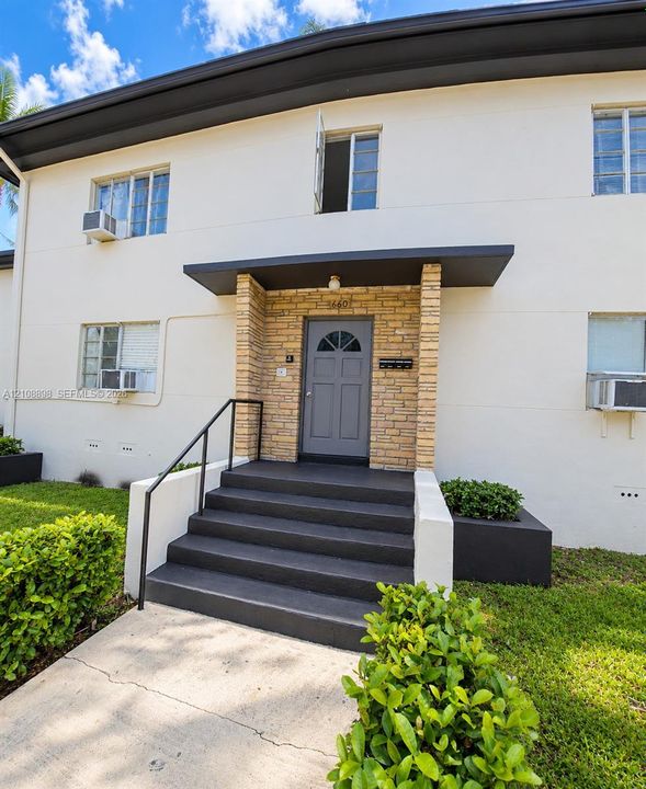 Exterior facade featuring a smooth stucco finish, stone-veneer entryway accents, gray-painted concrete stairs with metal handrails, and built-in landscape planters