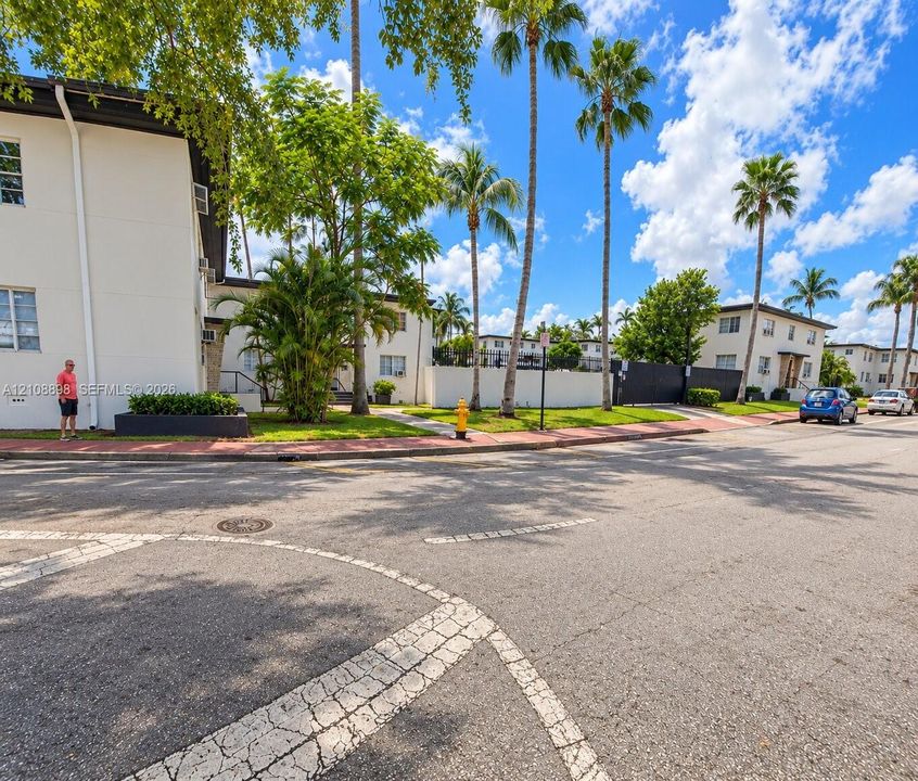 Exterior view of low-rise residential buildings featuring white stucco facades, mature palm trees, landscaped grounds, and paved street-level access