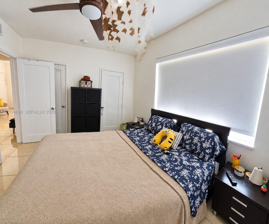 Room featuring neutral tile flooring, a ceiling fan with integrated lighting, dual doors with satin-finish hardware, and a large window equipped with a light-filtering roller shade