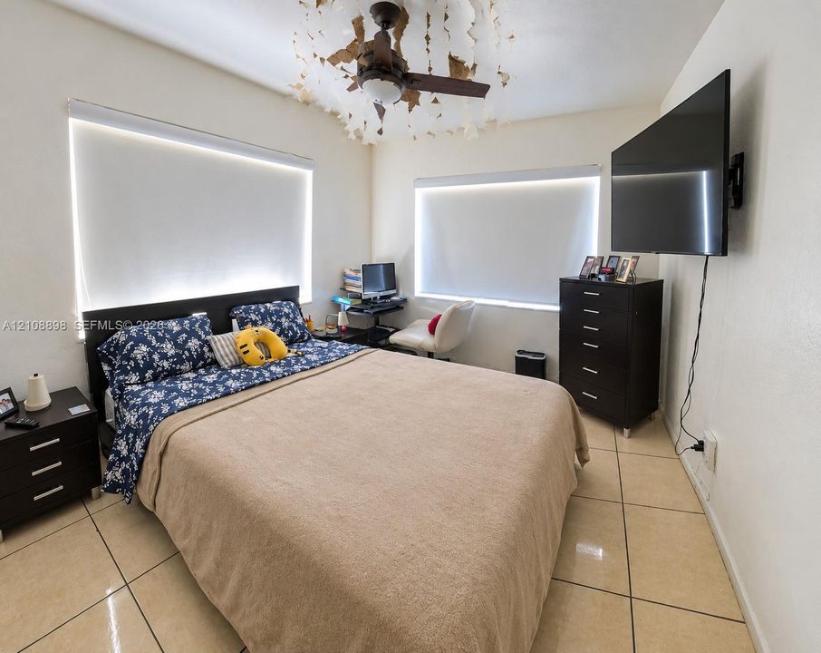 Tile flooring, multi-paneled ceiling fan with decorative light fixture, and two windows featuring motorized roller shades