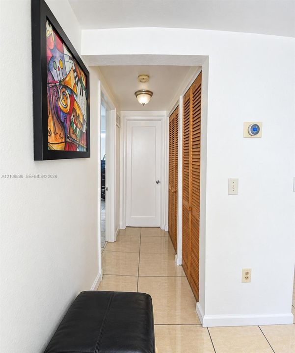 Hallway featuring large-format tile flooring, double louvered wood-finish closet doors, a classic shaker-style interior door, and a ceiling-mounted light fixture